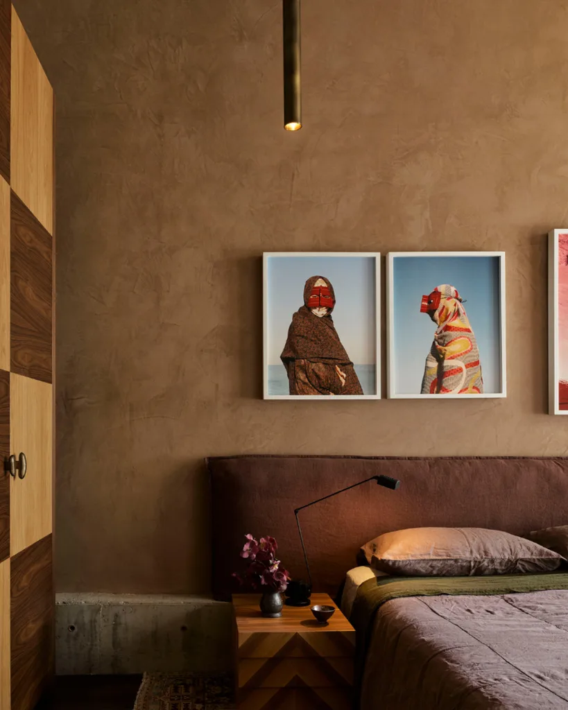 Beige rendered wall bedroom with check timber joinery and contemporary photographs hanging about the bed covered in linen.