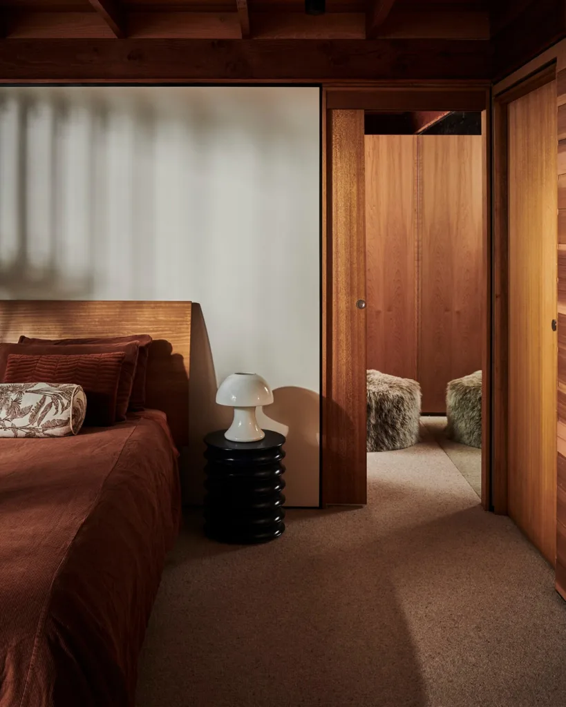 A timber-clad bedroom with a white mushroom lamp on a bedside table