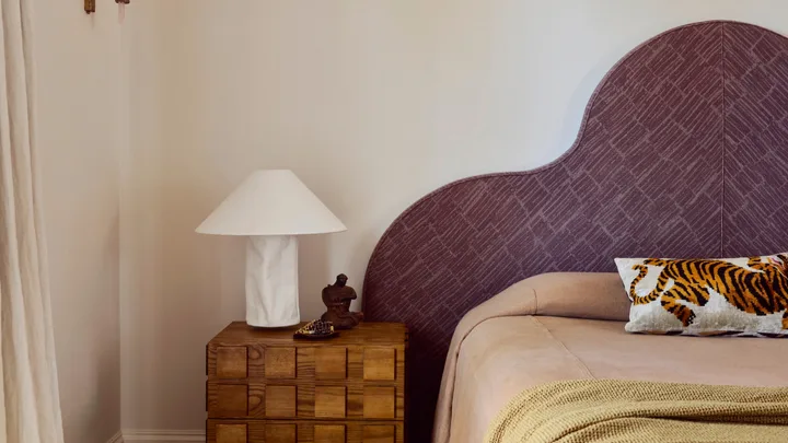 Cream bedroom with a plum bedhead, Cultiver linen, vintage bedside table, and a sisal carpet.