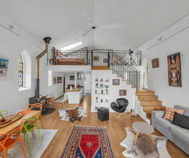 the interior of a converted church for sale in Berridale Australia with white walls, a loft bedroom and modern furniture.