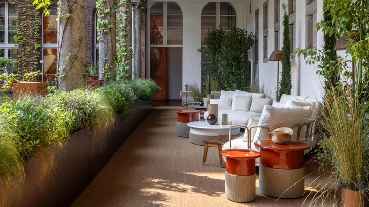 An alfresco balcony with white lounge furniture and orange and cord side tables flanked by greenery.