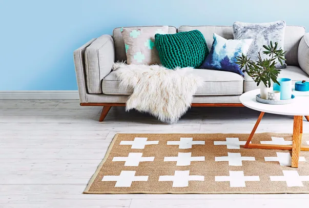 Modern living room with a gray sofa, colorful pillows, and a white fur throw, a patterned rug, and a round coffee table.