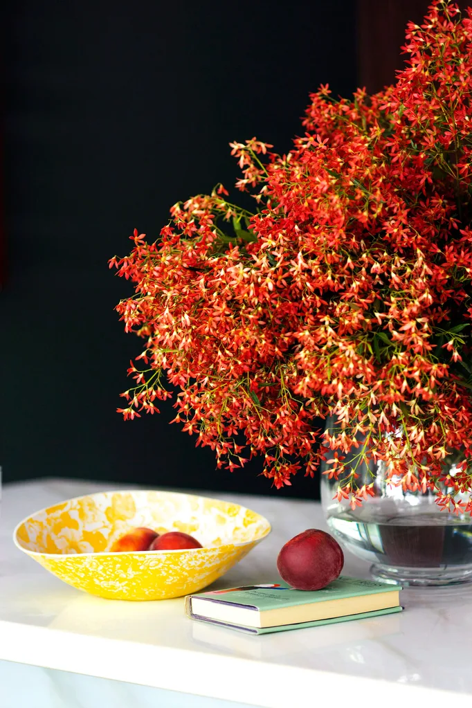 A sprig of flowers from a NSW Christmas bush in a vase beside a fruit bowl