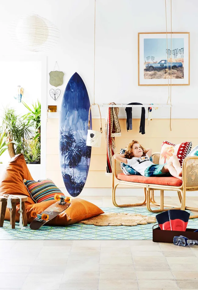 Child lounging in a bright, beach-themed room with a surfboard, skateboard, and vibrant decor.