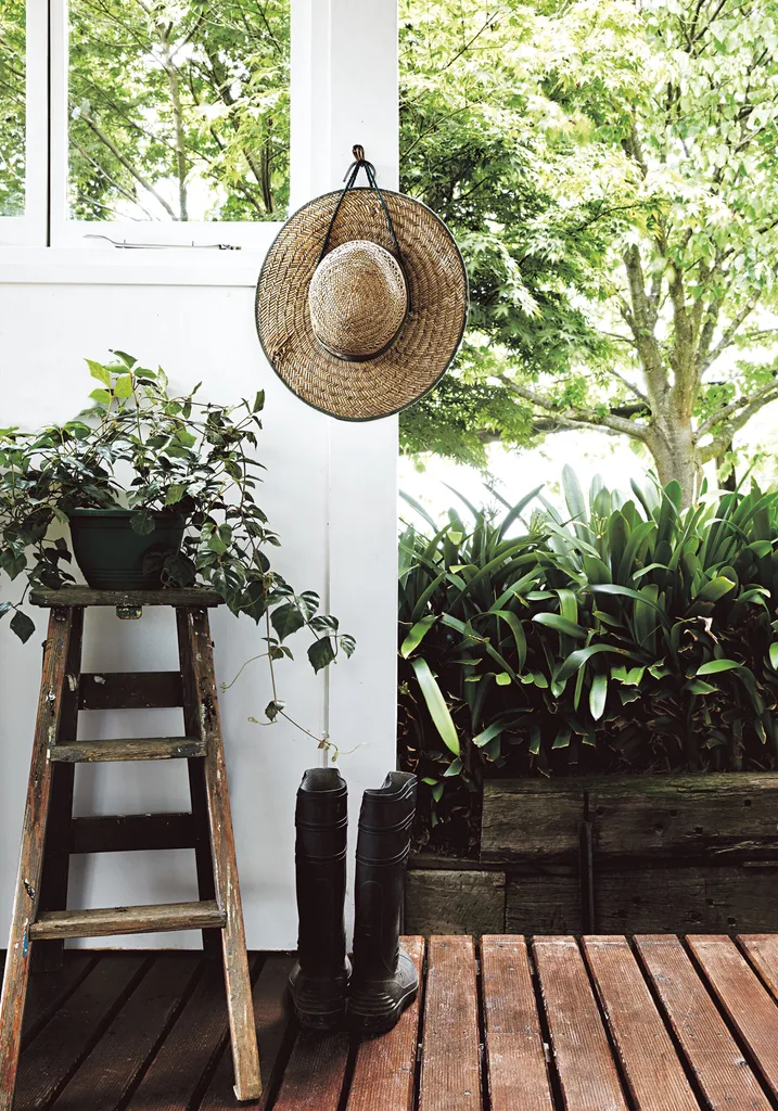 A shaded verandah with a timber deck, timber stool and hanging straw hat and welly boots