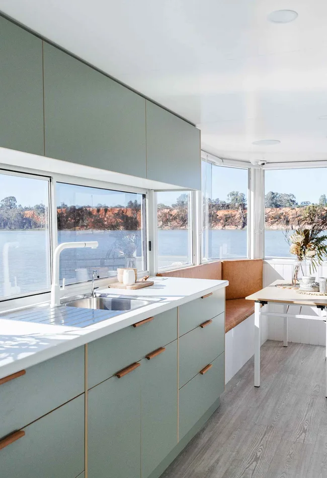 Modern houseboat kitchen with mint cabinets, a corner bench, and a view of a river through large windows.