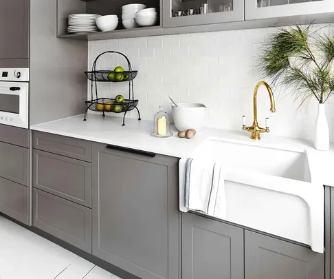 Modern kitchen with grey cabinets, a white countertop, gold faucet, farmhouse sink, and a basket of fruit.