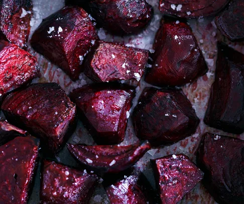 Close-up of roasted beetroot chunks sprinkled with coarse salt on a baking tray.