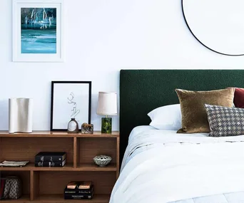 A bed with a green headboard, pillows, and bookshelf headboard with books, decor, and framed art on a white wall.