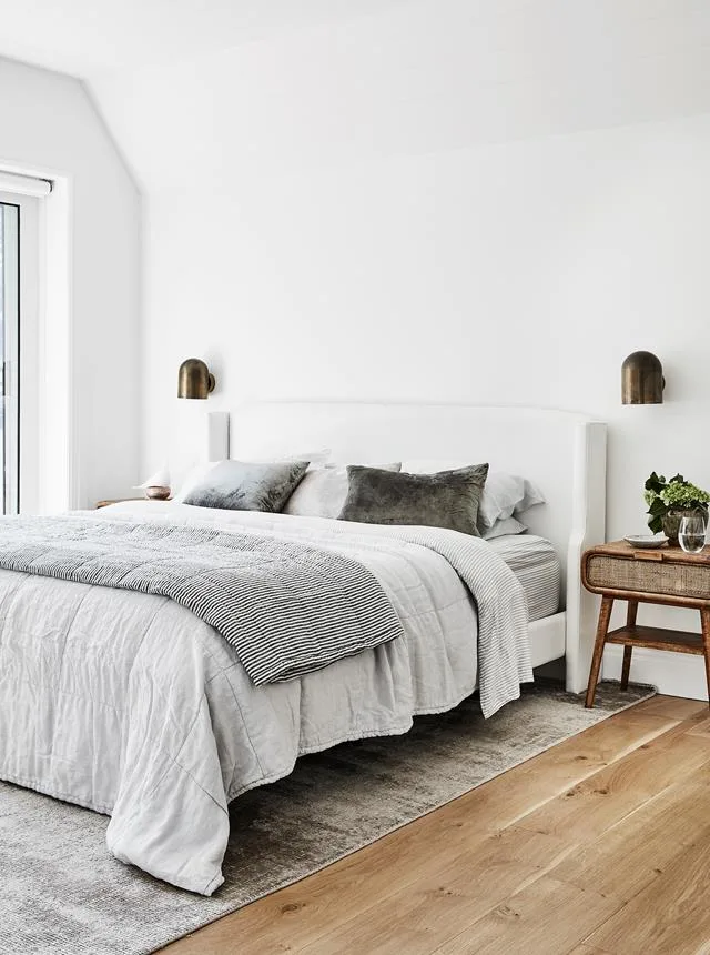 A light-filled bedroom with neutral bedding and white walls. 