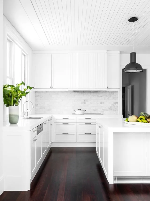 How to spring clean an open-plan white kitchen with dark timber flooring and a white subway tile splashback. 