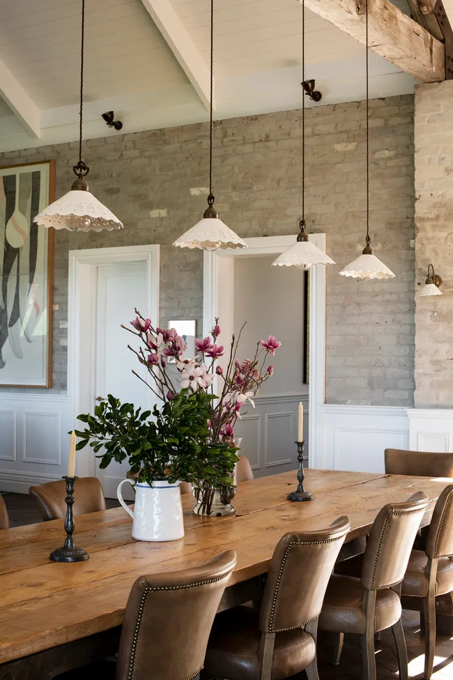 Dining room with wooden table, leather chairs, floral centerpiece, and hanging vintage pendant lights.