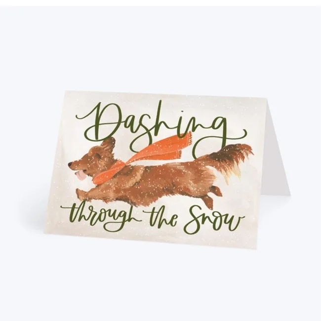 Greeting card with a dog wearing a red scarf, and the words "Dashing through the Snow" in green script.