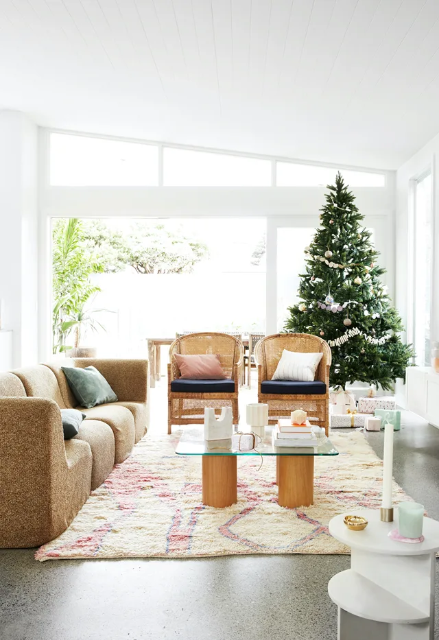 Modern living room with a Christmas tree, cozy sofa, rattan chairs, and a coffee table on a patterned rug.