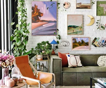 Living room with lush plants, cozy furniture, and colorful artwork on a white brick wall, creating a vibrant and eclectic decor.