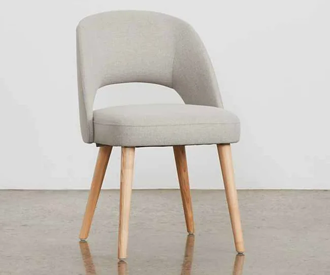 Gray upholstered chair with wooden legs on a shiny floor, against a plain background.