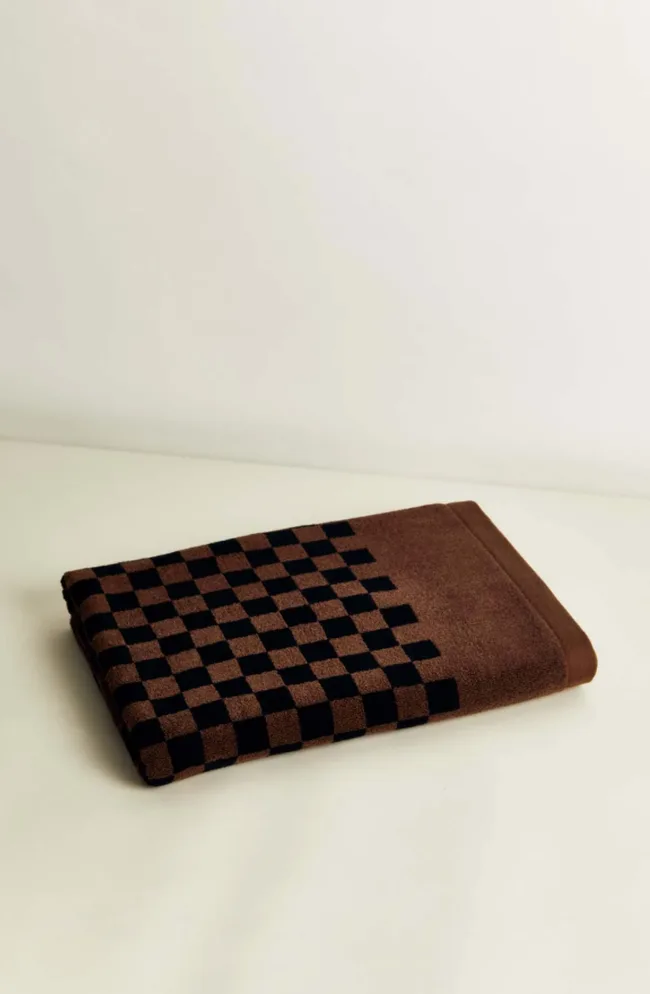 Brown towel with a black checkered pattern, folded neatly on a light surface.