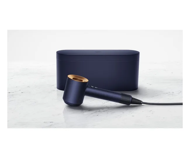 Navy blue Dyson Supersonic hair dryer with gold accents, placed on marble surface, next to a matching storage case.