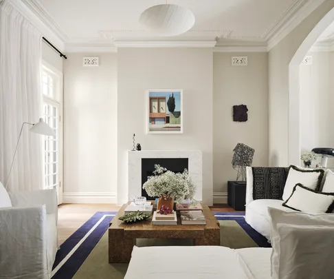 Luxurious living room with a white sofa, coffee table with flowers, abstract art, and modern decor.