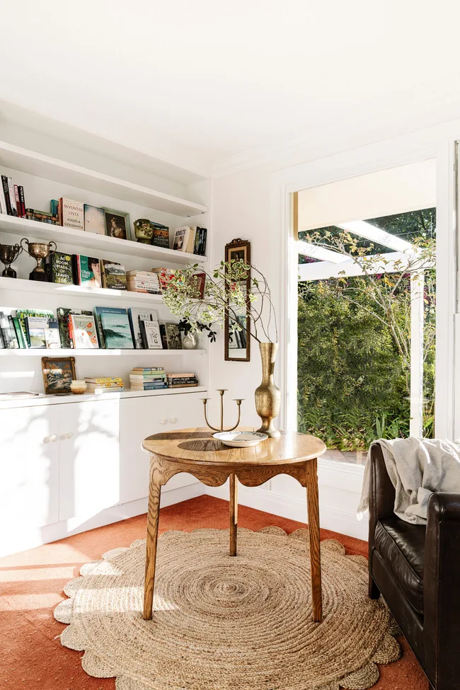 A library/sitting room with a round timber table and white shelving