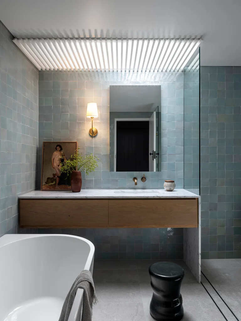 A modern blue bathroom with a wall sconce and marble and timber vanity