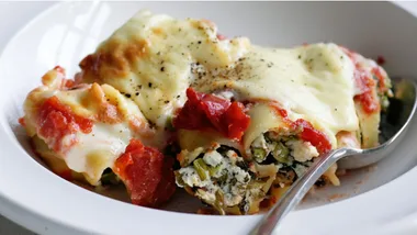 Ricotta and spinach cannelloni baked with béchamel sauce, topped with pepper and served in a white bowl with a spoon.