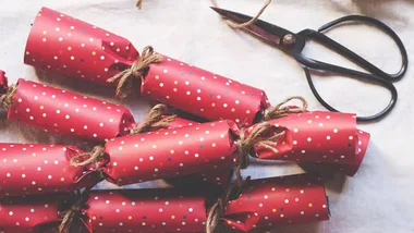 Red Christmas crackers with white polka dots and tied with twine beside a pair of black scissors on a table.